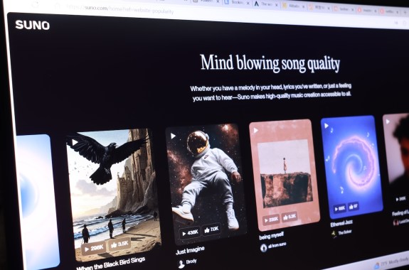 The Suno website on a computer screen with a black background and a carousel of song art.