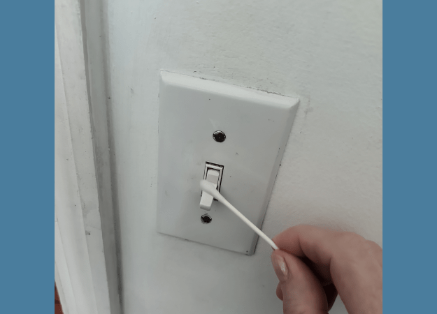A person holds a cotton swab against a light switch.
