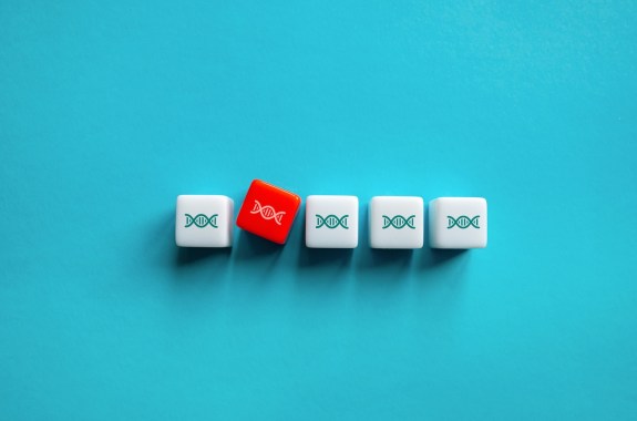 A row of white dice with small DNA illustrations. One red die with DNA is offset from the line.