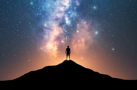 Milky Way and sporty man on mountain peak at starry night.