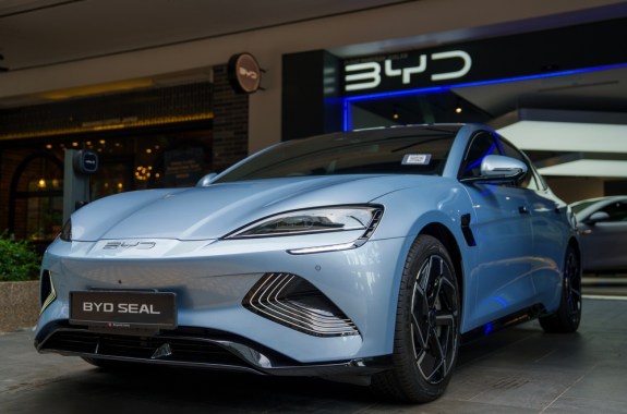 A light blue BYD Seal electric vehicle on display outside a BYD showroom, highlighting its sleek, futuristic design and front features.