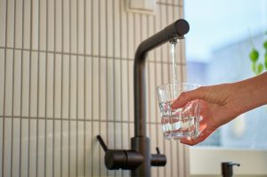 Hand filling glass with drinking water from kitchen faucet in modern home interior.