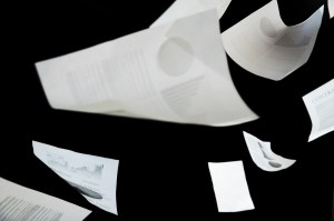 White papers with writing on them flutter through the air against a black background.