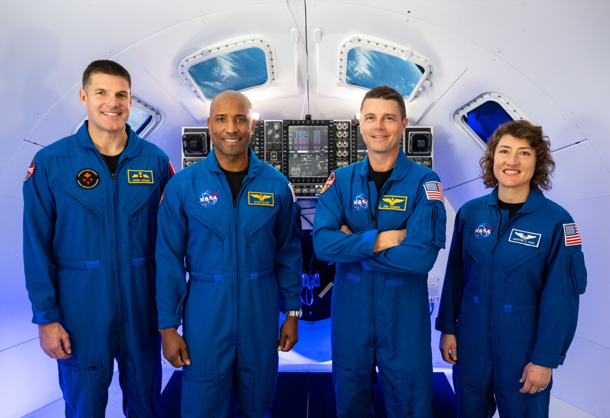 Official portrait of the four Artemis II crew members standing together in blue flight suits inside a spacecraft mock-up.