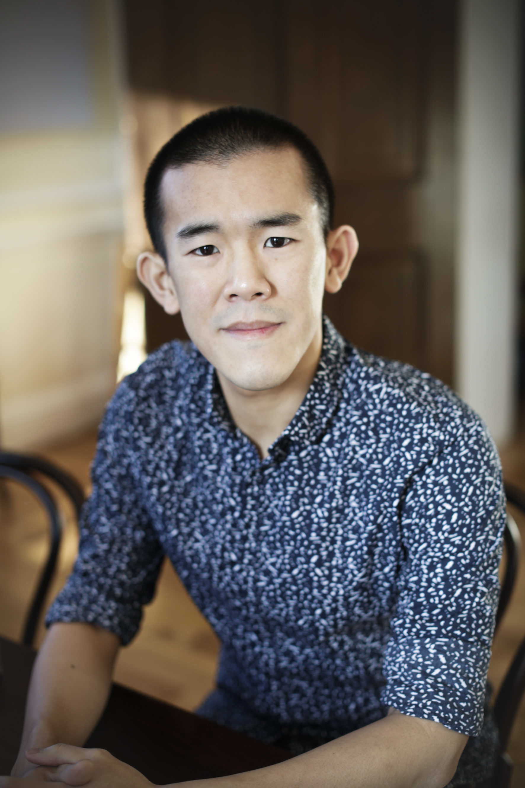 A portrait photo of a young man with short, cropped black hair and dark eyes wearing a blue patterned shirt.