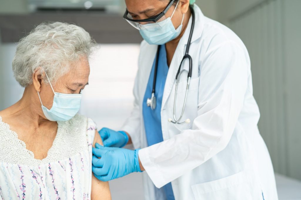Elderly Asian senior woman wearing face mask getting covid-19 or coronavirus vaccine by doctor make injection