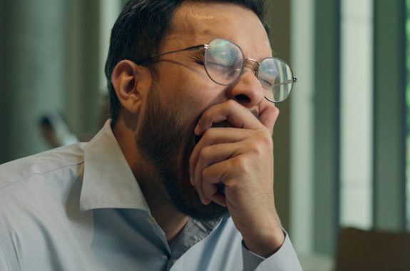 Man with glasses yawning and covering mouth with hand