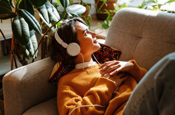 Brunette young woman listening music while resting on couch at home