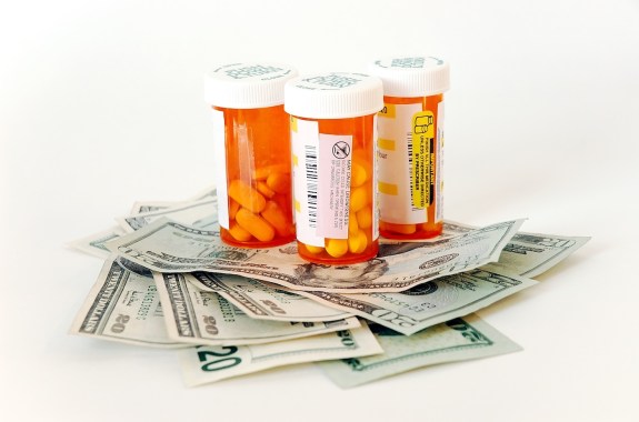 Three orange prescription pill bottles sit on a pile of $20 bills