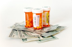 Three orange prescription pill bottles sit on a pile of $20 bills