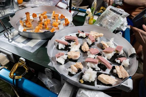 One tray features shrimp cocktail on whole grain wheat crackers, while the other holds sushi made with seaweed, spam, tuna, and rice.