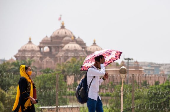 New Delhi, India- May 9 2022: man with umbrella crossing akshardham temple during heat wave condition in delhi