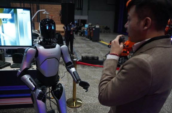 A black humanoid robot standing in front of a screen facing a man