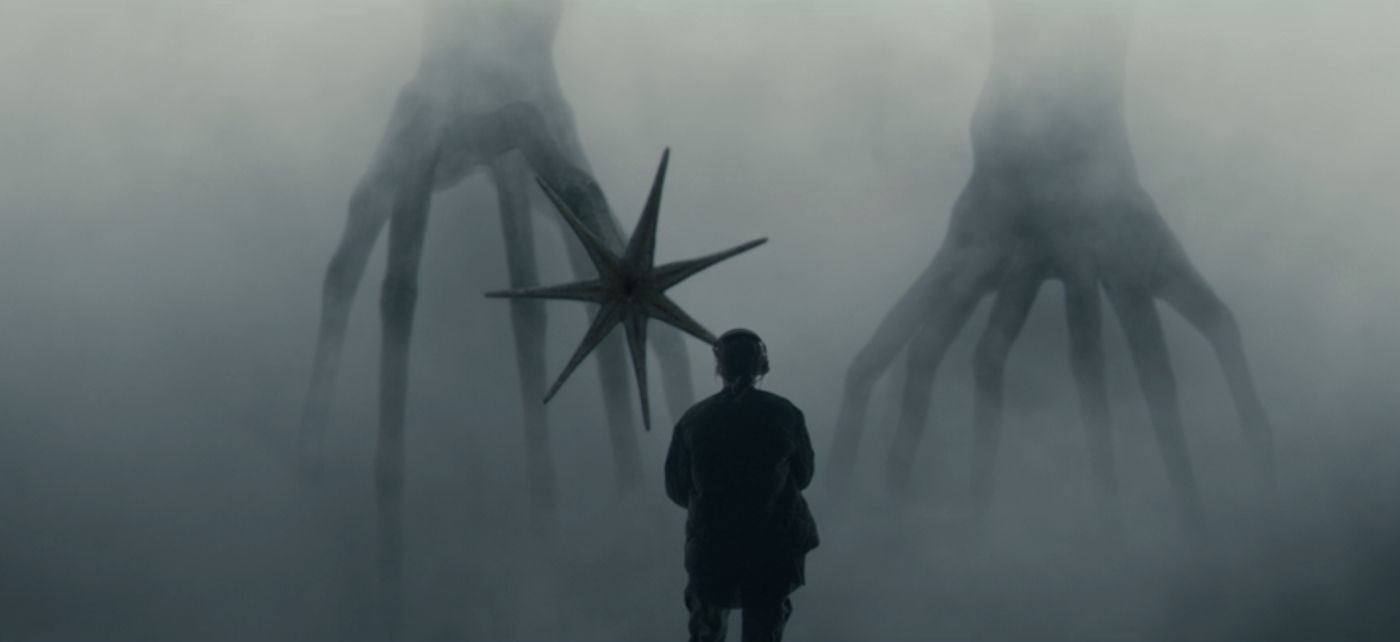 A silhouette of a woman in front of a hazy background with giant tree-root like creatures.