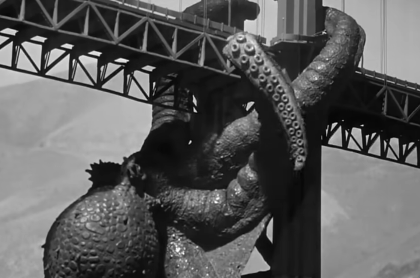 Black-and-white movie image showing a giant octopus wrapping its arms around a metal bridge