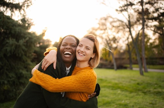 Two young women smile and hug in an sunny park